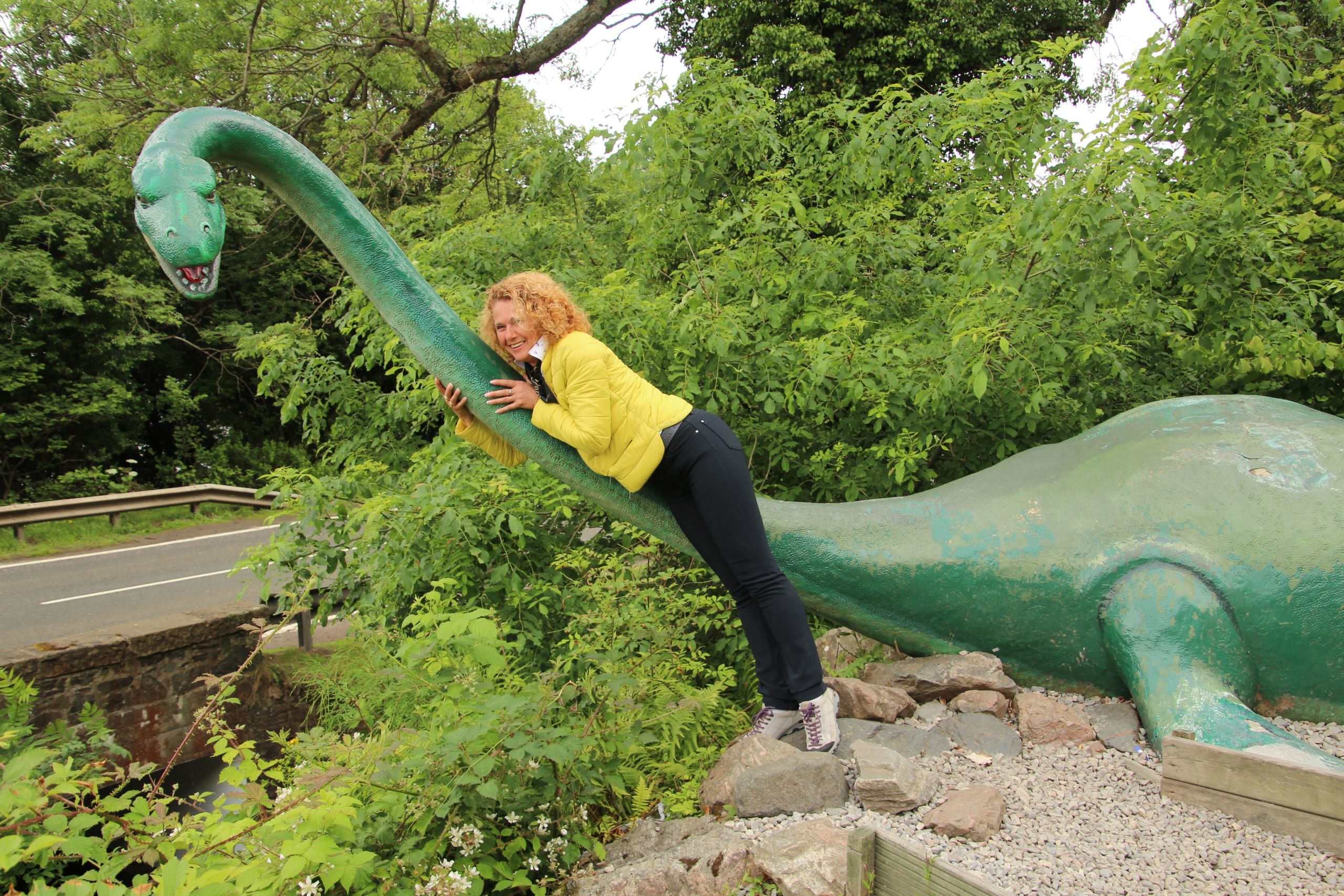 Turista abbraccia un finto mostro di Loch Ness a Drumnadrochit vicino al lago, immersa nel verde della natura scozzese lungo il Great Glen Way.